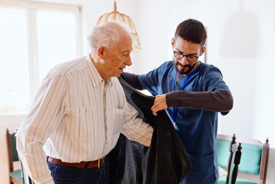 Home health aide helps an older man put on his coat