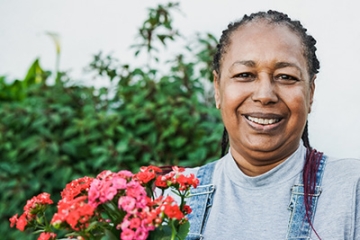 Older woman, with dementia, in the garden holding a pot of red flowers.